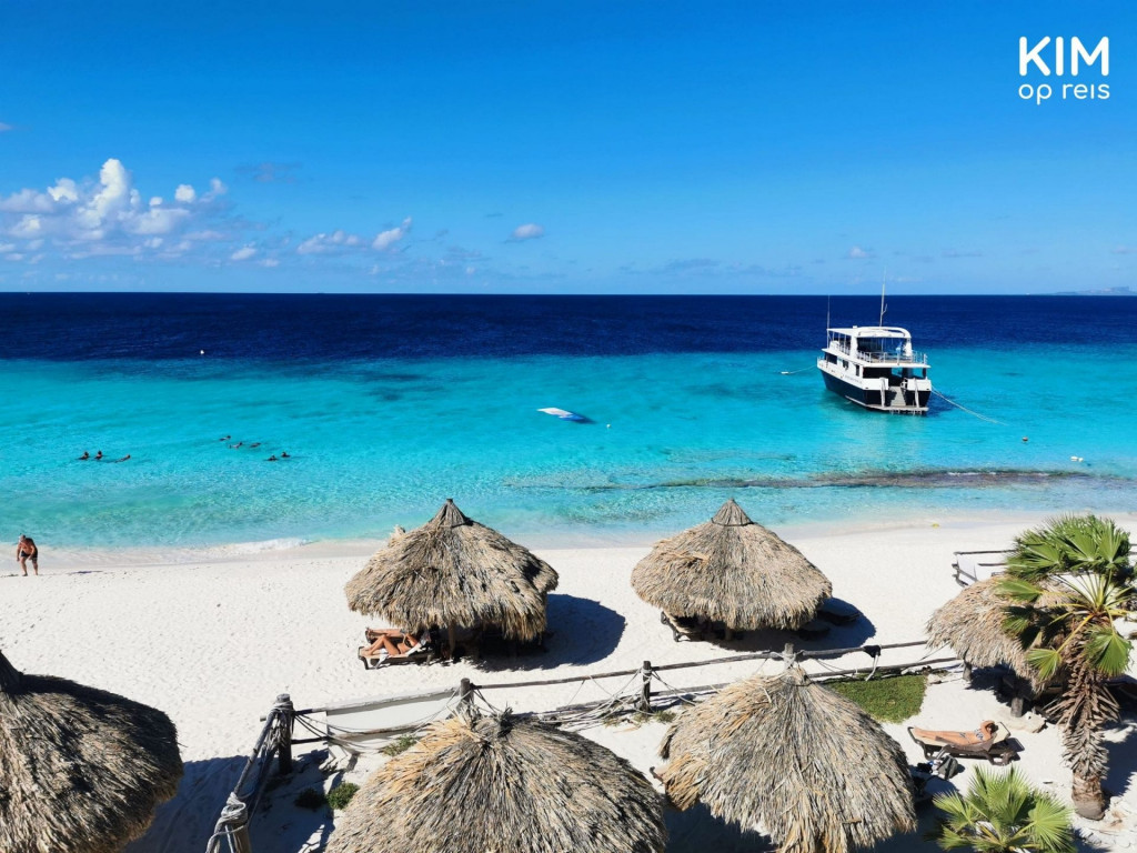 Bovenaanzicht Mermaid Beach House: strand met grote parasols en op de achtergrond de Mermaid boot in het water